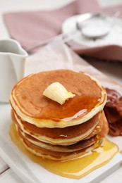 Photo of Delicious pancakes with maple syrup, butter and fried bacon on white table, closeup