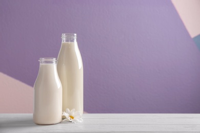Photo of Two bottles of fresh milk on table against color background