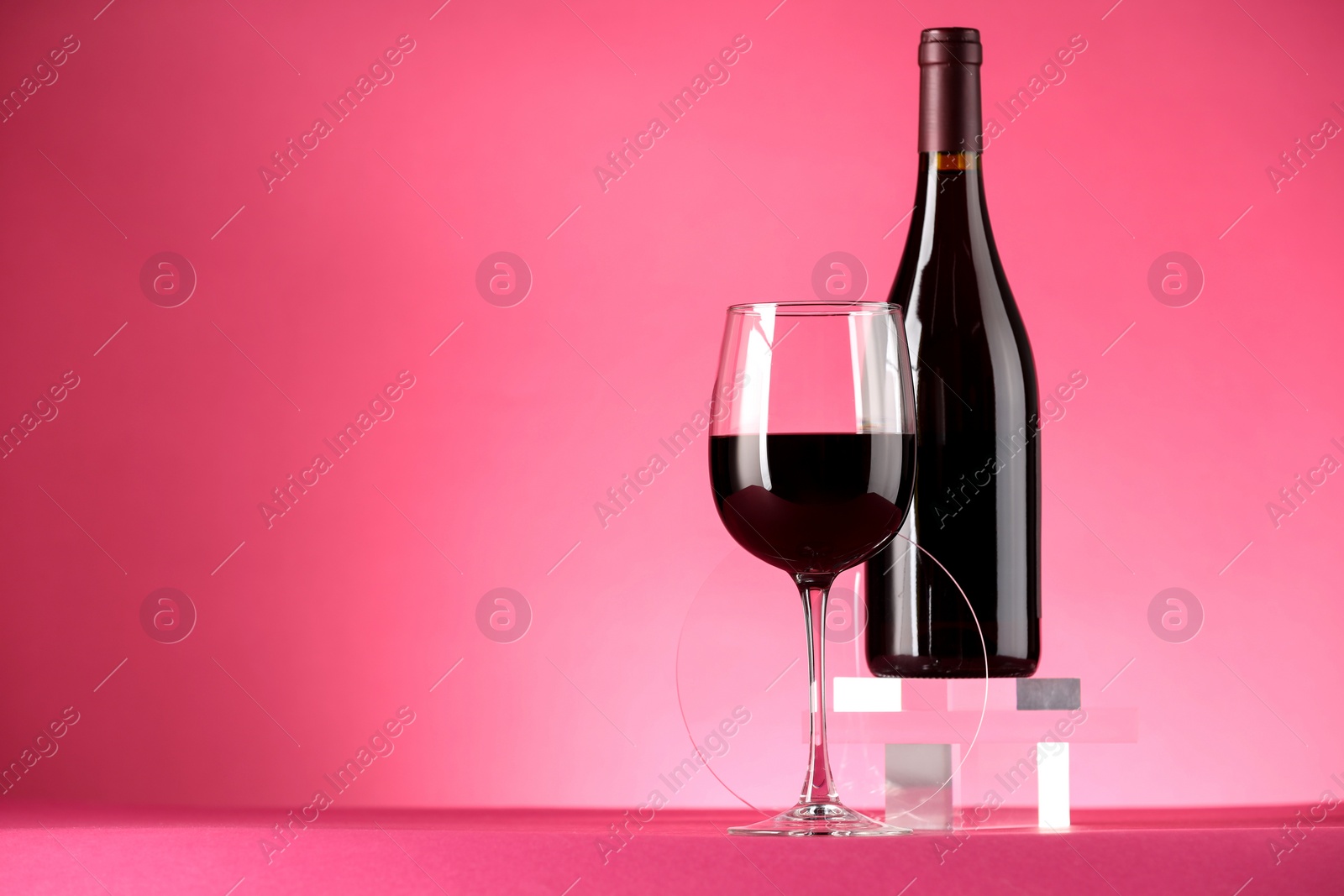 Photo of Stylish presentation of delicious red wine in bottle and glass on pink background. Space for text