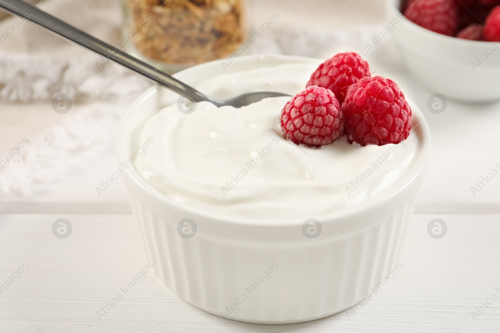 Photo of Yogurt served with raspberries on white wooden table, closeup
