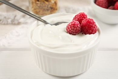 Photo of Yogurt served with raspberries on white wooden table, closeup