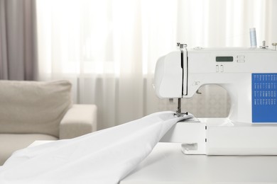 Photo of White sewing machine and fabric on table indoors, closeup