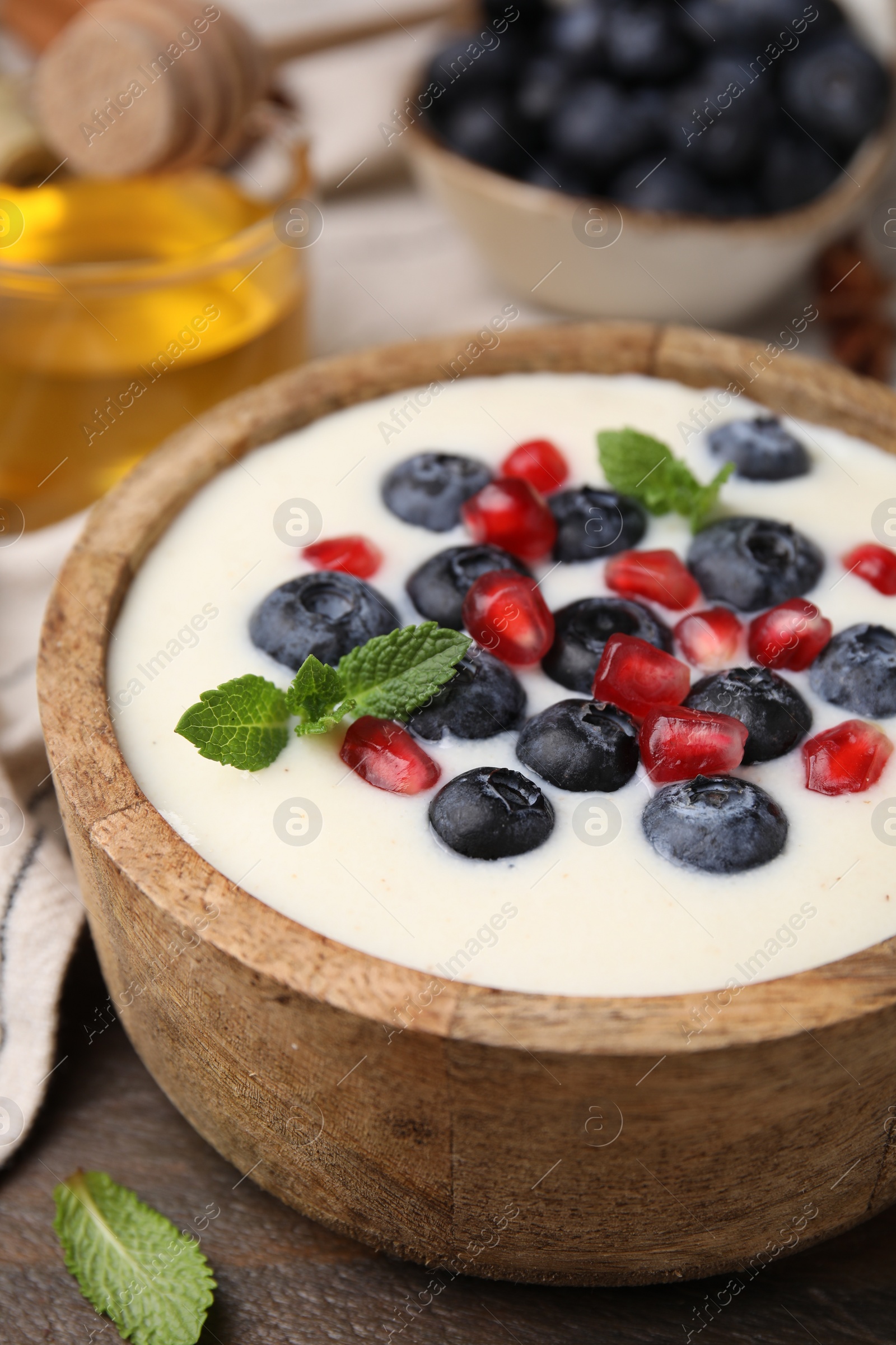 Photo of Bowl of delicious semolina pudding with blueberries, pomegranate and mint on table, closeup