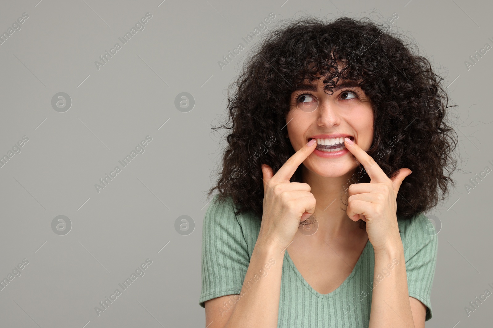 Photo of Young woman applying whitening strip on her teeth against grey background, space for text