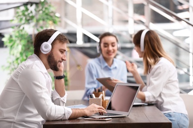 Photo of Young businessman with headphones, laptop and his colleagues at table in office