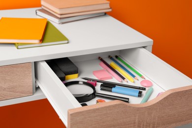 Office supplies in open desk drawer on orange background
