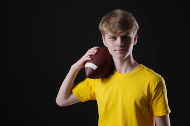 Photo of Teenage boy with american football ball on black background. Space for text