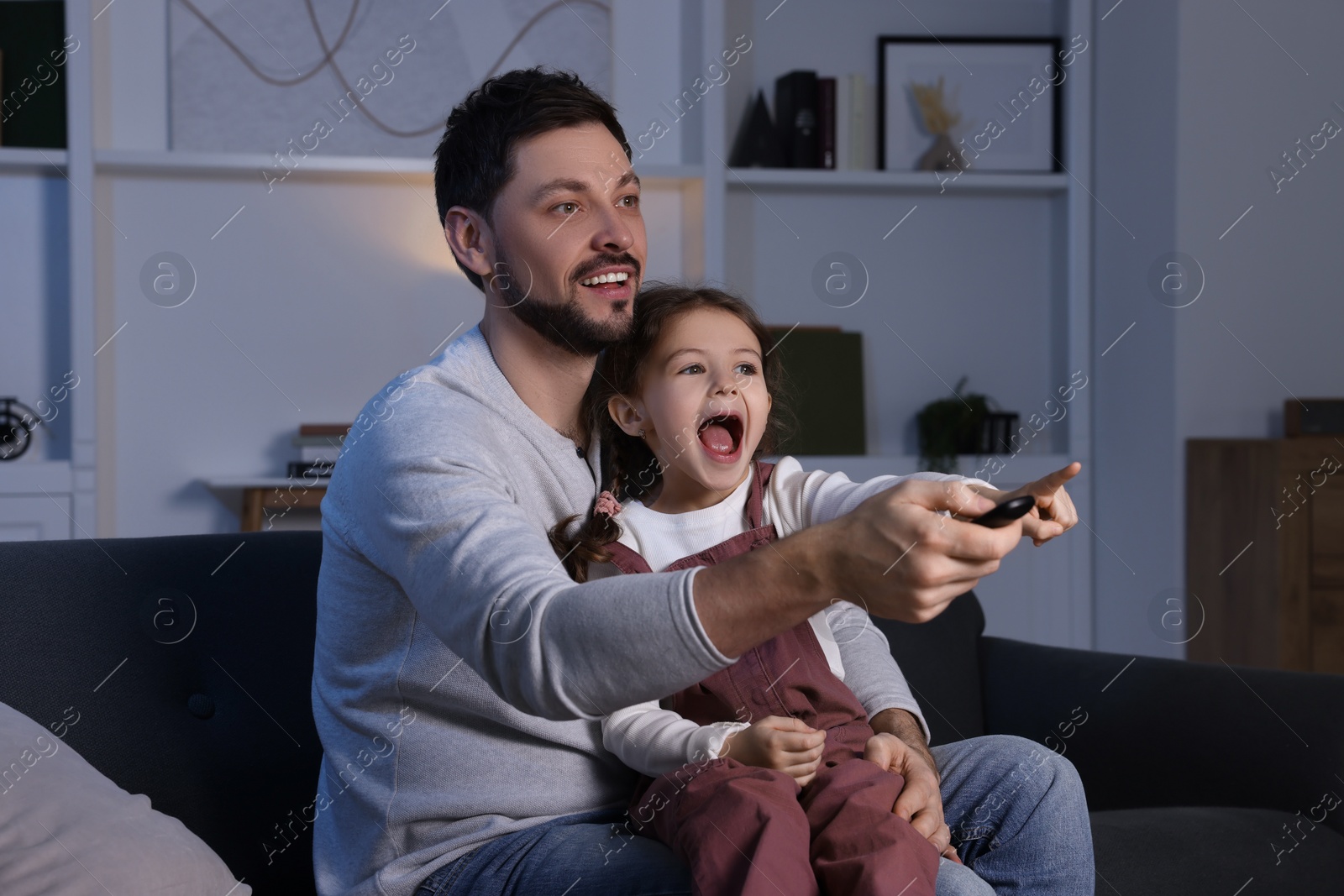 Photo of Father and daughter spending time near TV at home. Happy man holding remote control