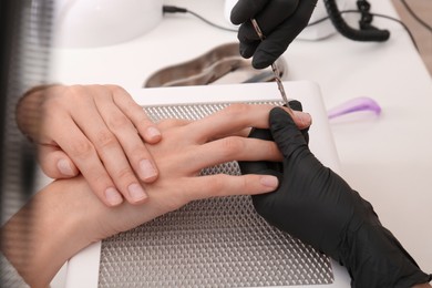 Photo of Professional manicurist working with client at white table, closeup