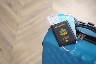 Photo of Passport with protective mask and tickets on light blue suitcase, space for text. Travel during quarantine