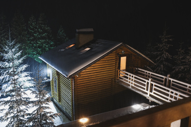 Photo of Wooden cottage with snowy yard at night, above view. Winter vacation