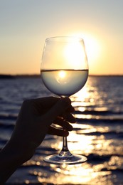 Photo of Woman holding glass of wine near river at sunset, closeup