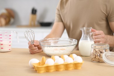 Photo of Man with whisk and different ingredients at table in kitchen, closeup. Online cooking course