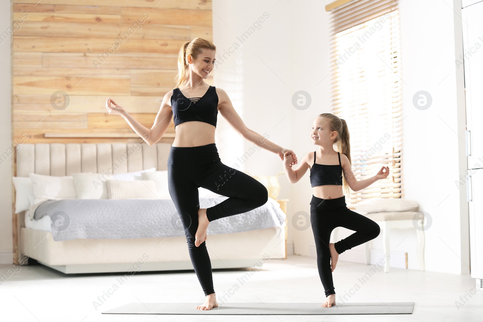 Photo of Mother and daughter in matching sportswear doing yoga together near bed at home