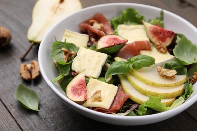 Photo of Tasty salad with brie cheese, prosciutto, pear and figs on wooden table, closeup