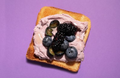 Photo of Tasty sandwich with cream cheese, blackberries and blueberries on lilac background, top view