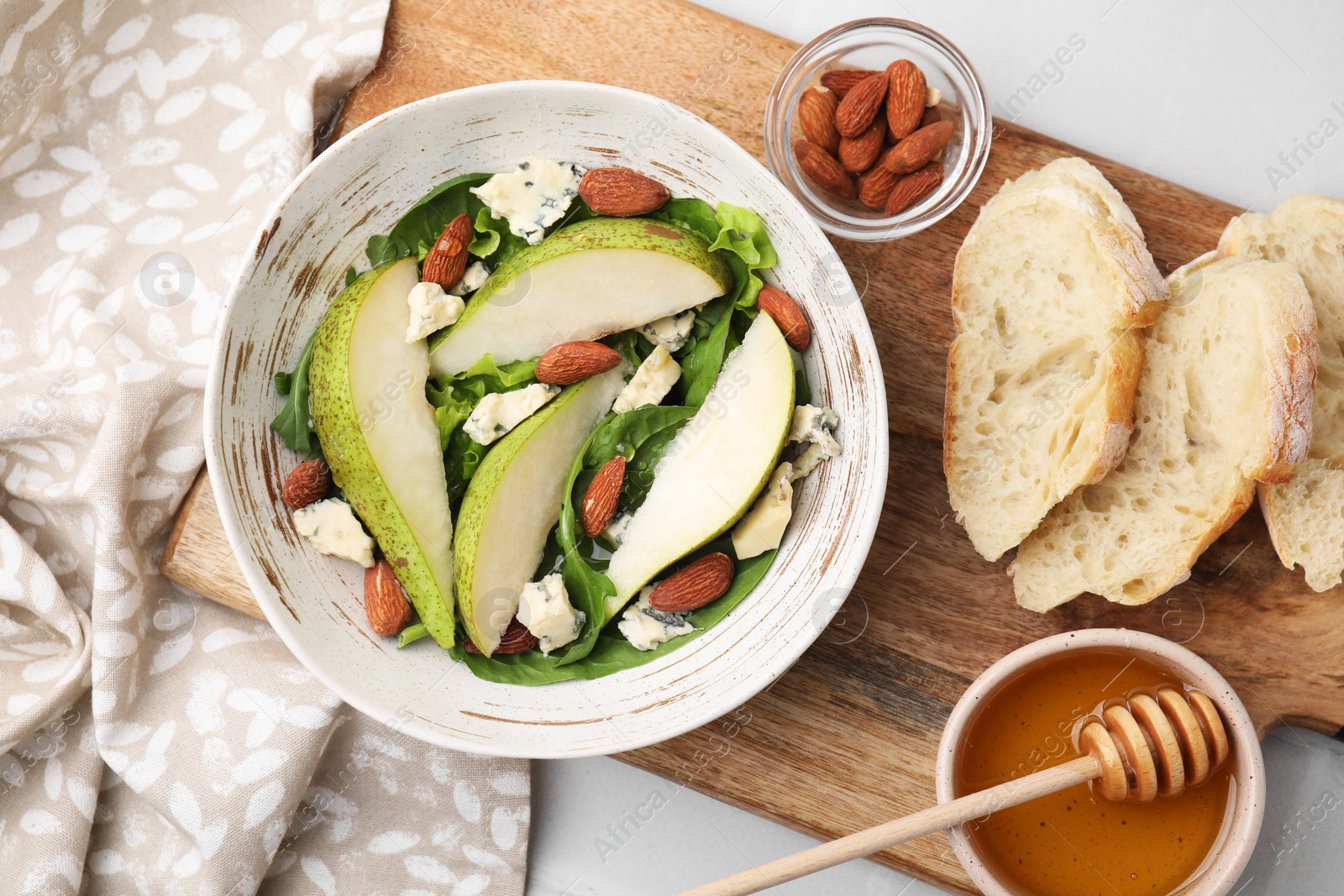 Photo of Delicious pear salad in bowl, honey and bread on light table, top view