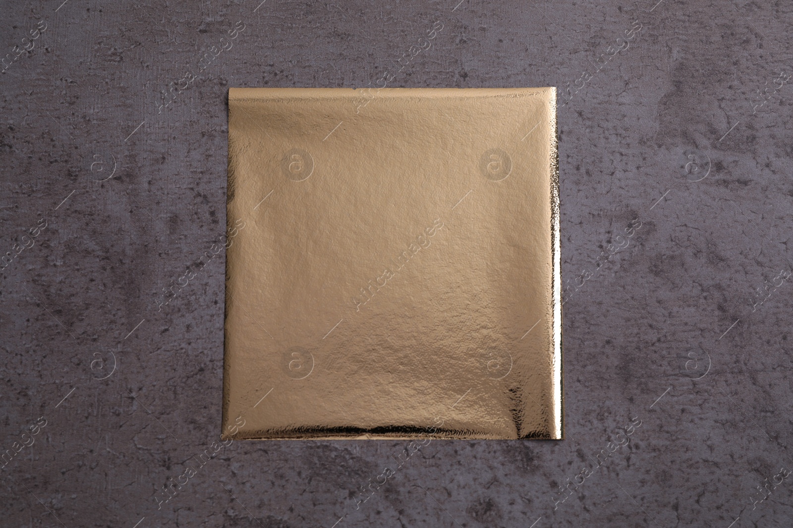 Photo of Edible gold leaf sheet on grey textured table, top view