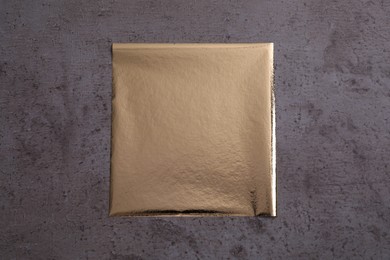 Photo of Edible gold leaf sheet on grey textured table, top view