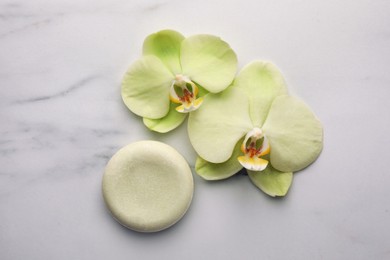 Solid shampoo bar and orchid flowers on white marble table, flat lay. Spa composition