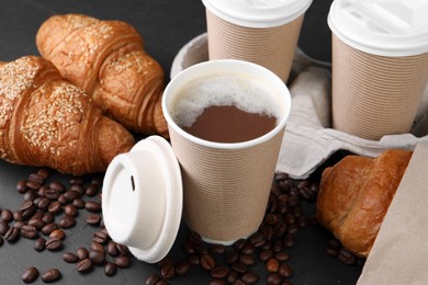 Photo of Coffee to go. Paper cups of tasty drink, croissants and beans on black table, closeup