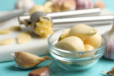 Photo of Fresh peeled garlic cloves in bowl on light blue wooden table, closeup. Organic product