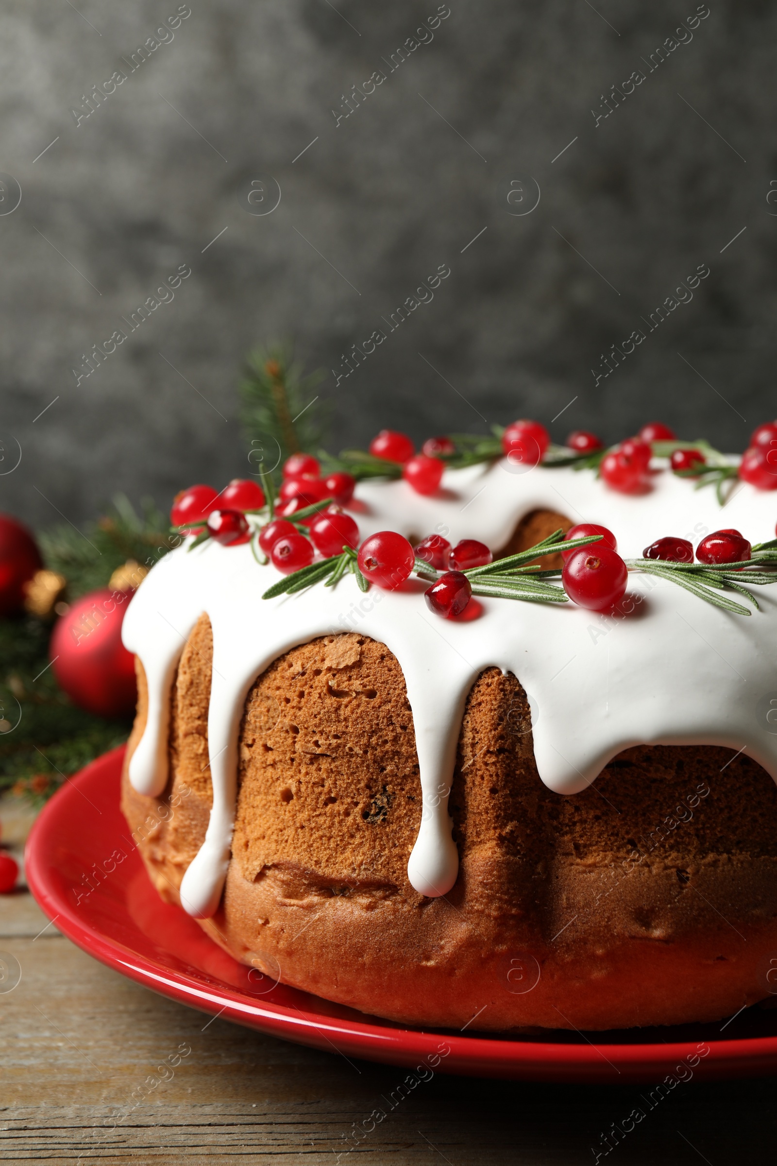 Photo of Traditional Christmas cake decorated with glaze, pomegranate seeds, cranberries and rosemary on wooden table