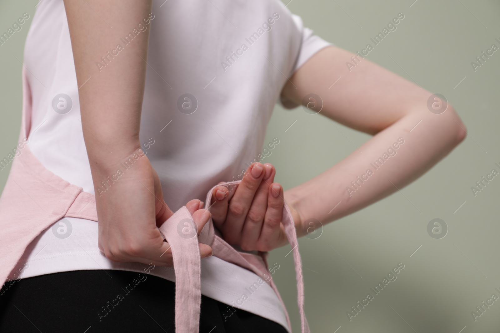 Photo of Woman putting on pink apron against light green background, closeup