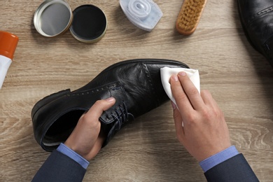 Photo of Man cleaning leather shoe at wooden table, top view