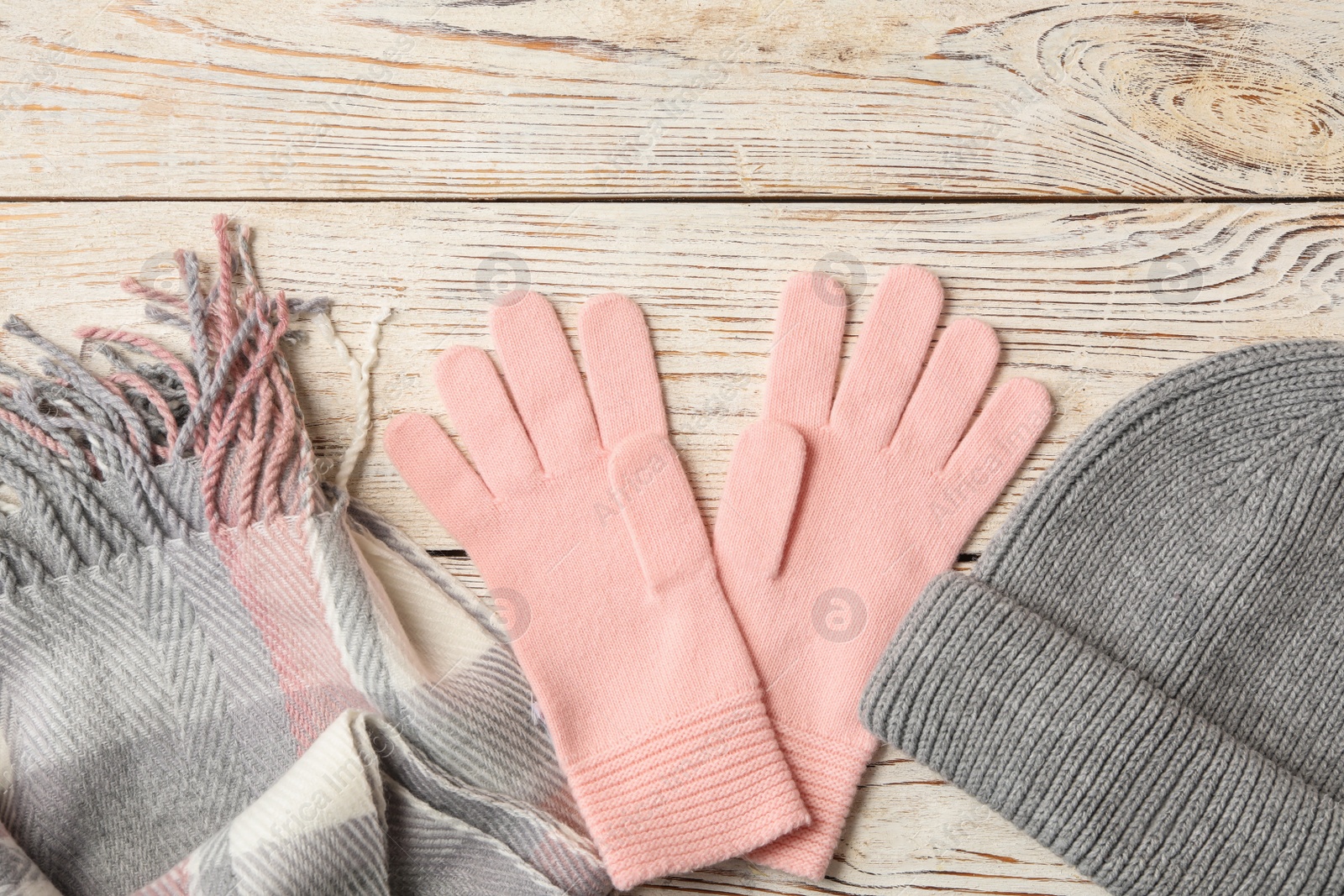 Photo of Stylish pink woolen gloves, scarf and hat on white wooden table, flat lay