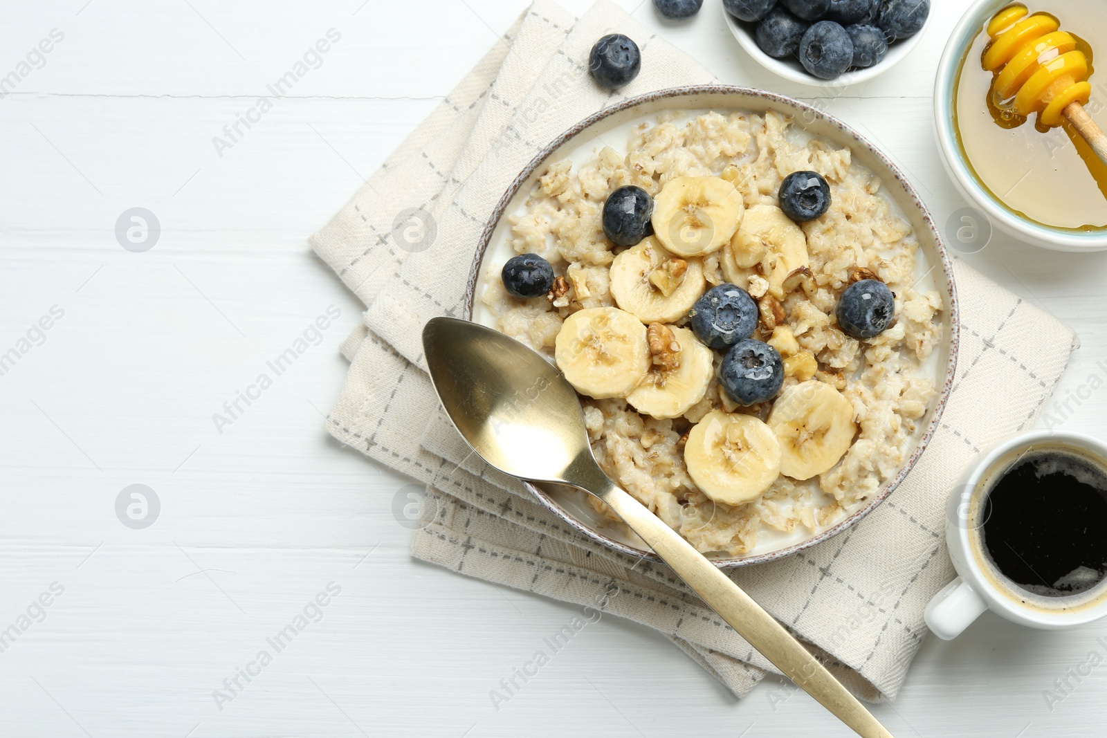 Photo of Tasty oatmeal with banana, blueberries, walnuts and honey served in bowl on white wooden table, flat lay. Space for text