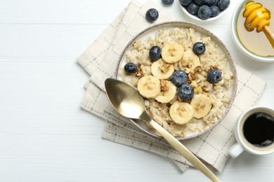 Tasty oatmeal with banana, blueberries, walnuts and honey served in bowl on white wooden table, flat lay. Space for text