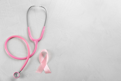 Photo of Pink ribbon and stethoscope on light grey stone background, flat lay with space for text. Breast cancer concept