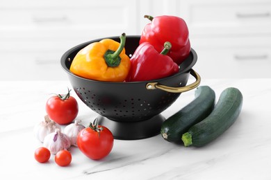 Photo of Black colander and different vegetables on white marble table, closeup