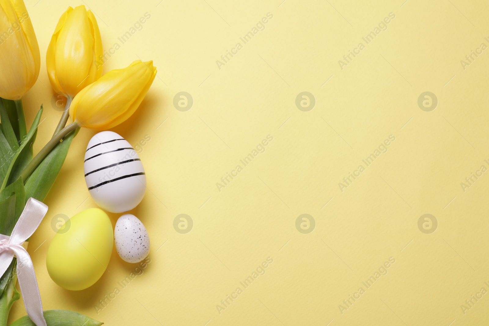 Photo of Flat lay composition with tulips and beautifully painted eggs on yellow background, space for text. Easter celebration