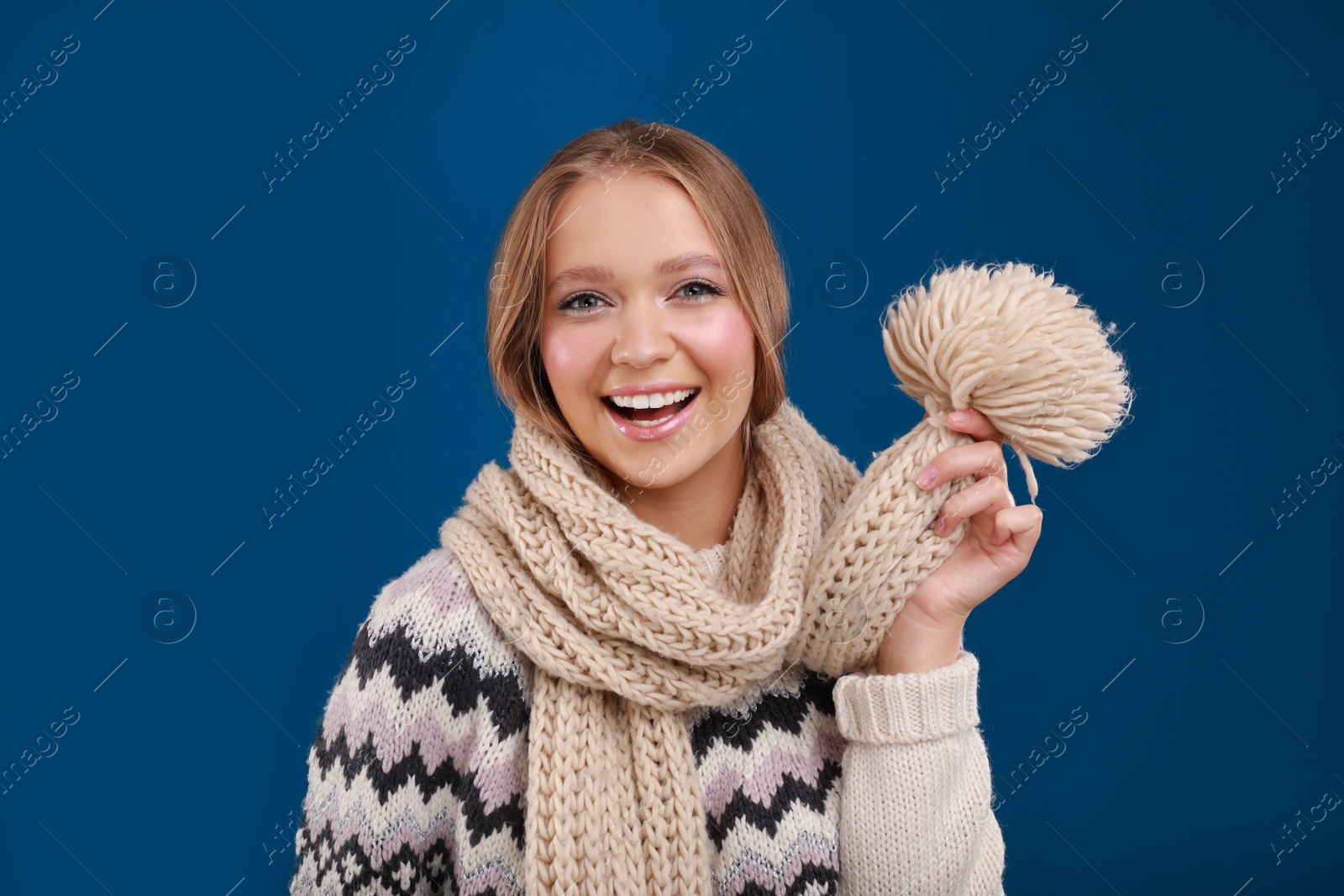 Photo of Young woman in warm sweater and scarf on blue background. Winter season