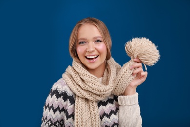 Young woman in warm sweater and scarf on blue background. Winter season