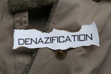 Photo of Piece of burnt paper with word Denazification on grey jacket, top view