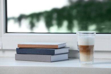 Books and glass with latte on white window sill