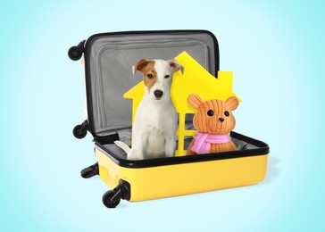Image of Cute dog toy bear and model of house in suitcase on light blue background