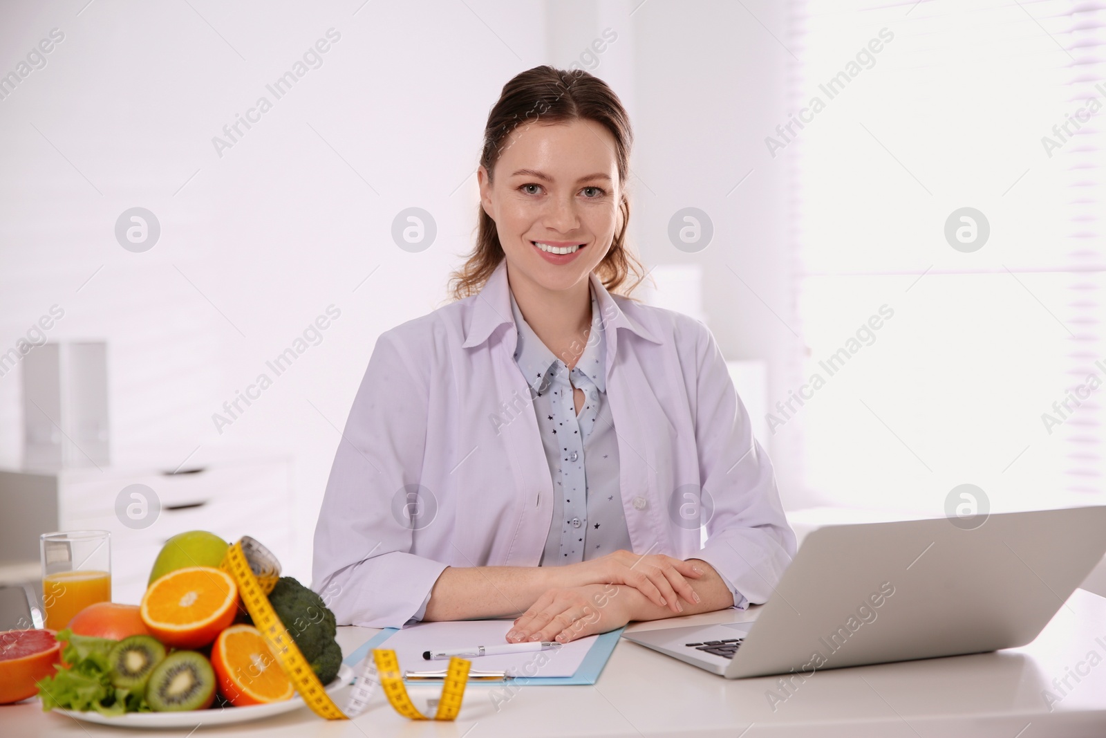 Photo of Nutritionist with clipboard and laptop at desk in office