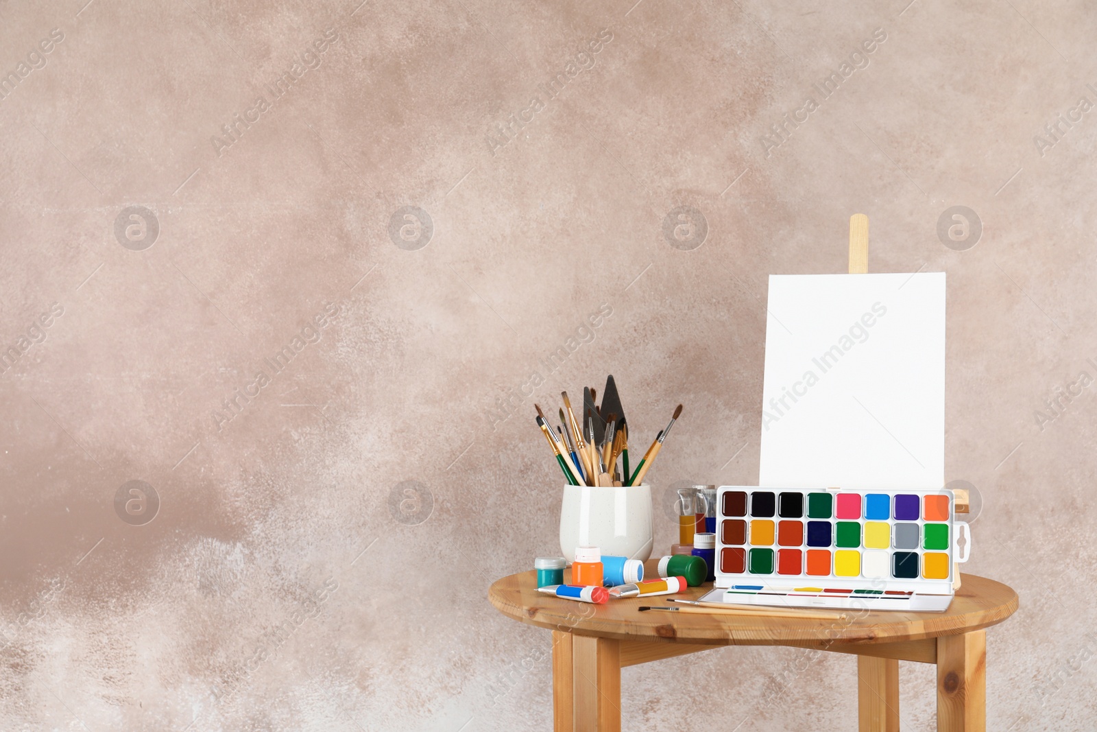 Photo of Wooden easel with blank canvas board and painting tools for children on table near color wall. Space for text