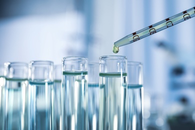 Dripping reagent into test tube with liquid sample on blurred background, closeup. Laboratory analysis