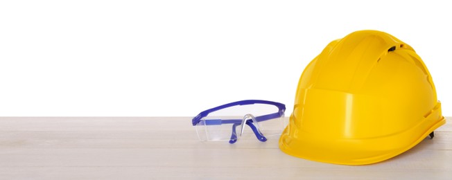Photo of Hard hat and goggles on light wooden table against white background. Safety equipment