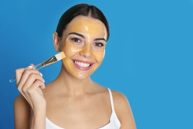 Young woman applying cleansing mask on her face against color background. Space for text