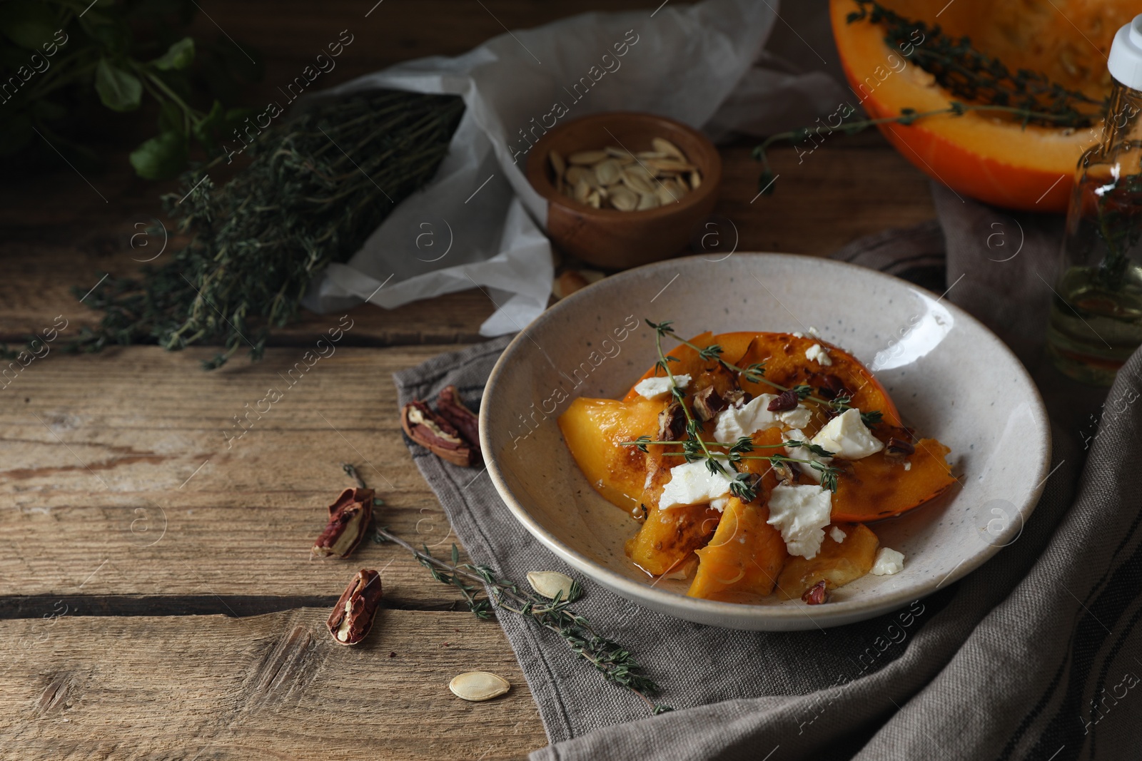 Photo of Baked pumpkin slices served with cheese, thyme and pecans on wooden table, space for text