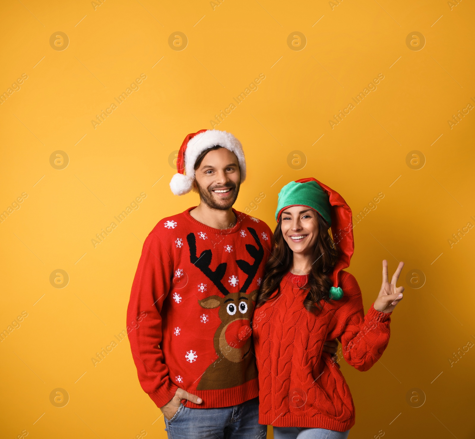 Photo of Young couple in Christmas sweaters and hats on yellow background. Space for text