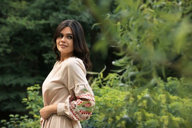 Beautiful woman wearing embroidered dress in countryside, space for text. Ukrainian national clothes