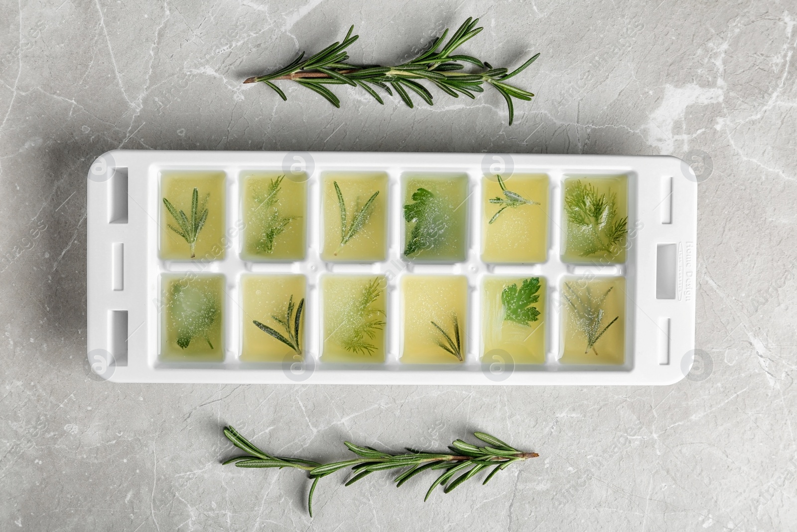 Photo of Ice cube tray with herbs frozen in oil and fresh rosemary on grey background, flat lay