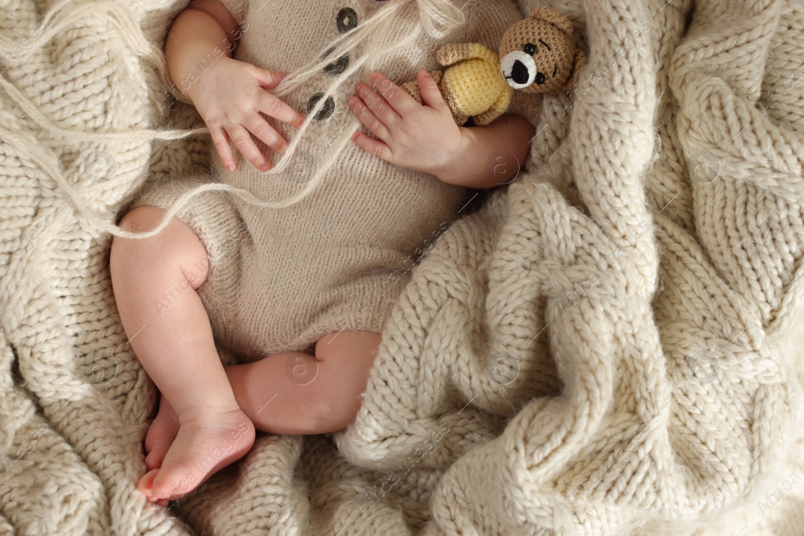 Photo of Top view of adorable newborn baby with toy bear on knitted plaid, closeup